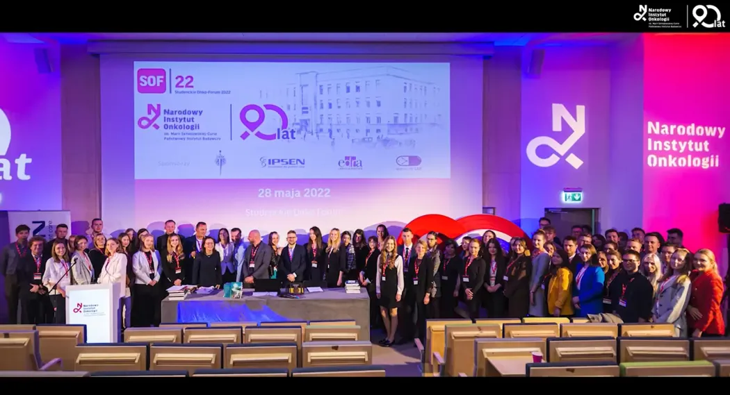 Grupa ludzi w auli, w tle ekran z logo SOF, Narodowego Instytutu Onkologii i datą 28 maja 2022