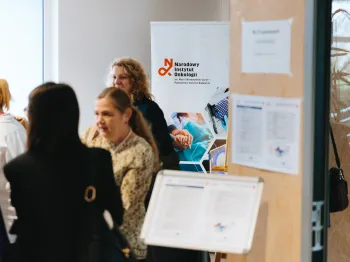 Grupa osób stoi przed banerem Narodowego Instytutu Onkologii w pomieszczeniu konferencyjnym.