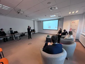 Osoby siedzące w sali konferencyjnej, jedna osoba stoi przy ekranie z prezentacją.