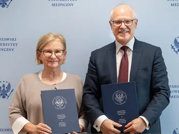 Dwie osoby trzymające teczki z logo Warszawskiego Uniwersytetu Medycznego na tle z jego nazwą.