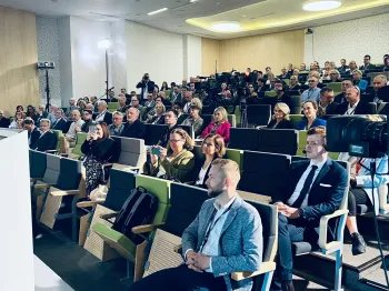 Ludzie siedzący w audytorium, słuchający prezentacji lub wykładu.