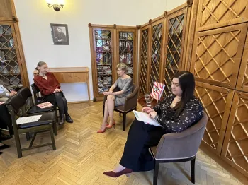 Trzy osoby siedzą w sali z drewnianymi regałami, jedna z nich trzyma książkę.