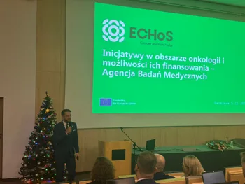 Mężczyzna przemawia przy podium obok choinki; slajd z napisem: „Inicjatywy w obszarze onkologii i możliwości ich finansowa…