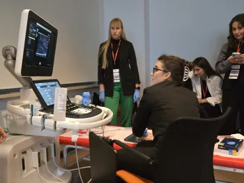 Osoby przy aparacie do ultrasonografii, jedna siedzi, inne stoją, patrzą na ekran.