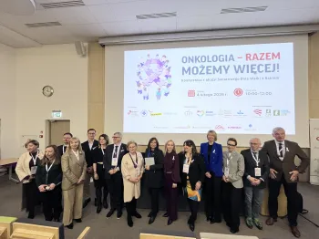 Grupa osób pozuje przed ekranem z napisem: 