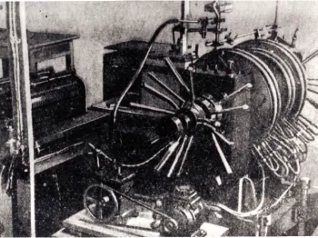 Czarno-białe zdjęcie dużego elektromagnesu z widocznymi cewkami i przewodami w laboratorium.