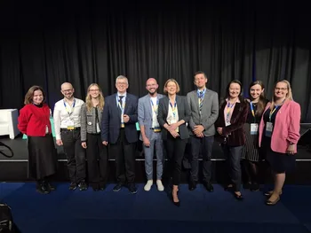 Grupa dziesięciu osób pozuje na tle ciemnej kurtyny, wszyscy ubrani formalnie.