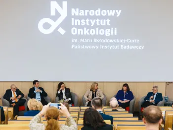 Panel dyskusyjny z sześcioma osobami na scenie, logo Narodowego Instytutu Onkologii w tle