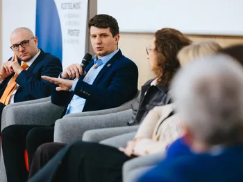 Mężczyzna z mikrofonem mówi podczas panelu dyskusyjnego, obok siedzą inni uczestnicy.