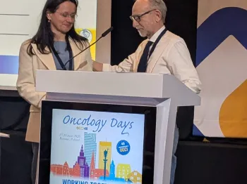 Dwie osoby przy mównicy, ekran z napisem „Oncology Days” i informacjami o wydarzeniu.