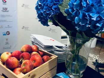 Kosz z jabłkami, wazon z niebieskimi hortensjami, ulotki i plakat Narodowego Instytutu Onkologii