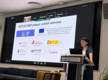 Kobieta przy mównicy, w tle slajd z logotypami i tekstem o projekcie WCT EVI MAP.