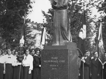 Pomnik Marii Skłodowskiej-Curie z napisem „Mari Skłodowskiej Curie Stolica 1935”, wokół stoją ludzie z flagami.
