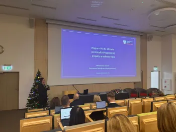 Sala konferencyjna, osoba prezentuje slajd o programie UE dla zdrowia, projekty w zakresie raka.