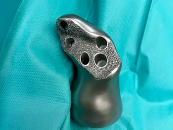 Metalowy implant z kilkoma otworami na tle turkusowego materiału chirurgicznego.