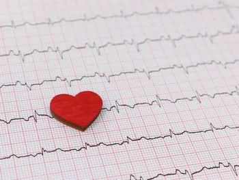 Drewniane czerwone serce na tle wykresu EKG z widocznymi liniami fal.