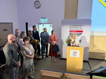 Grupa ludzi na sali konferencyjnej, obok plakat XII Warszawskiej Konferencji Onkologicznej.
