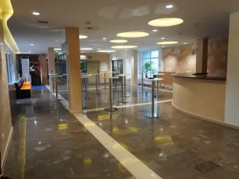 Hol z marmurową podłogą, stolikami koktajlowymi i ladą recepcyjną, jasne oświetlenie sufitowe.
