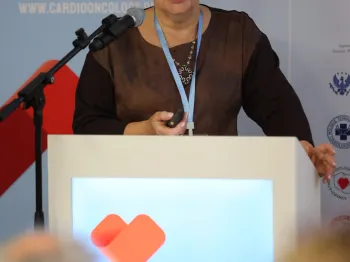 Kobieta przy mównicy z mikrofonem, w tle napis 