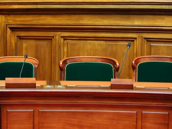Trzy puste krzesła przy drewnianym stole konferencyjnym z mikrofonami