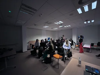 Grupa ludzi siedzących w sali konferencyjnej, niektórzy patrzą na ekran.