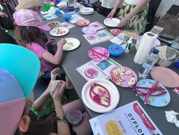 Dzieci dekorują ciasteczka przy stole na pikniku, obok leży dyplom.