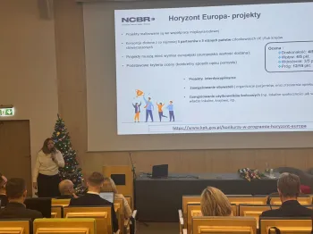 Prezentacja na temat projektów Horyzont Europa, kobieta przemawia, choinka w tle.