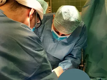 Dwóch chirurgów w sali operacyjnej podczas zabiegu, ubrani w zielone fartuchy i maski.