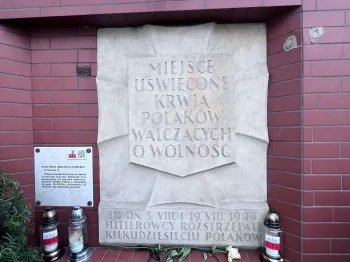 Tablica pamiątkowa z napisem o miejscu uświęconym krwią Polaków walczących o wolność, otoczona zniczami.