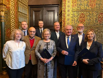 Grupa osób w eleganckich strojach pozuje w ozdobnym wnętrzu z bogato zdobionymi ścianami.