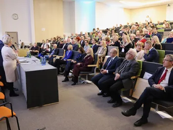 Sala konferencyjna z publicznością, osoby siedzą na krzesłach, z przodu stoi prelegentka.