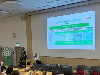 Osoba prezentuje slajd na temat Polish Cancer Mission Hub w sali wykładowej z choinką.