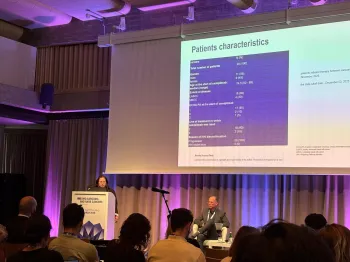 Prezentacja w sali konferencyjnej, kobieta przy mównicy, slajd z tabelą „Patients characteristics”.