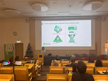 Sala wykładowa, prelegentka przy mównicy, na ekranie slajd o strukturze organizacyjnej.