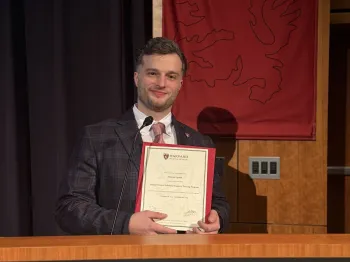 Mężczyzna w garniturze trzyma certyfikat na tle logo Harvard Medical School
