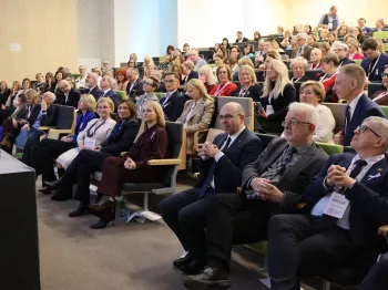 Ludzie siedzący w audytorium, niektórzy z identyfikatorami, patrzą w stronę sceny.