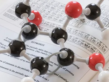 Model cząsteczki chemicznej na tle otwartej książki z układem okresowym pierwiastków.