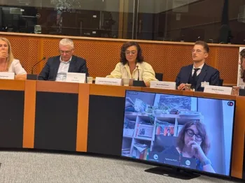 Osoby siedzące przy stole konferencyjnym, na ekranie widać osobę uczestniczącą zdalnie.