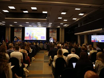 Konferencja w sali z ekranem, na którym widnieje napis 