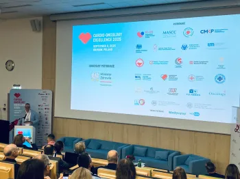 Konferencja Cardio-Oncology Excellence 2025, Warszawa. Prelegent przy mównicy, ekran z logotypami patronów.