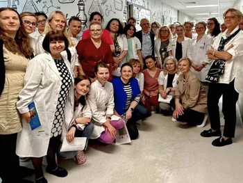 Grupa ludzi w korytarzu, część w białych fartuchach, na ścianie rysunki.
