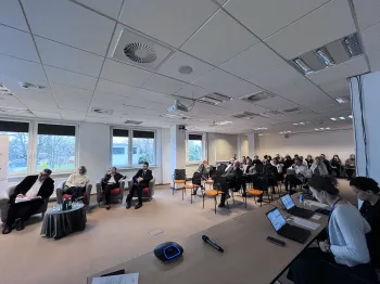 Sala konferencyjna z ludźmi siedzącymi na krzesłach, projektor, laptopy na stole