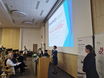 Prezentacja w sali konferencyjnej, kobieta przy mównicy, slajd z napisem 