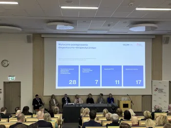 Sala konferencyjna, panel dyskusyjny, ekran z tekstem: „Wytyczne postępowania diagnostyczno-terapeutycznego”.