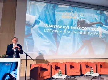 Mężczyzna przy mównicy, obok ekran z napisem 