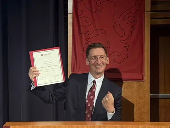 Mężczyzna w garniturze trzyma certyfikat na tle logo Harvard Medical School.