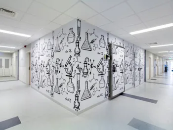 Korytarz w centrum onkologii z grafikami przedstawiającymi sprzęt laboratoryjny na ścianach.