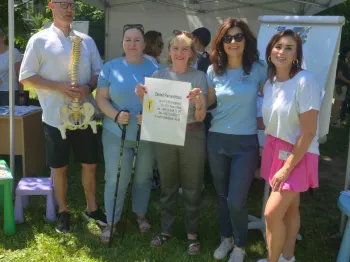 Grupa osób stoi przed namiotem na trawie, jedna osoba trzyma plakat.