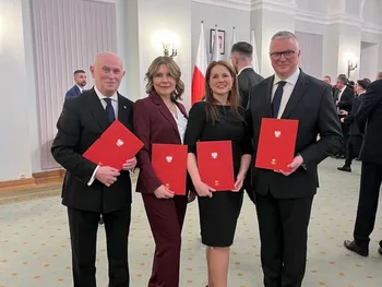Cztery osoby w eleganckich strojach trzymają czerwone teczki z godłem Polski, w tle flagi.