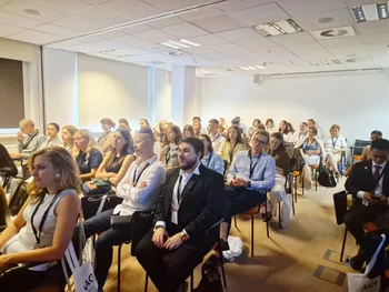 Grupa ludzi siedzących w sali konferencyjnej, większość z identyfikatorami na szyi.